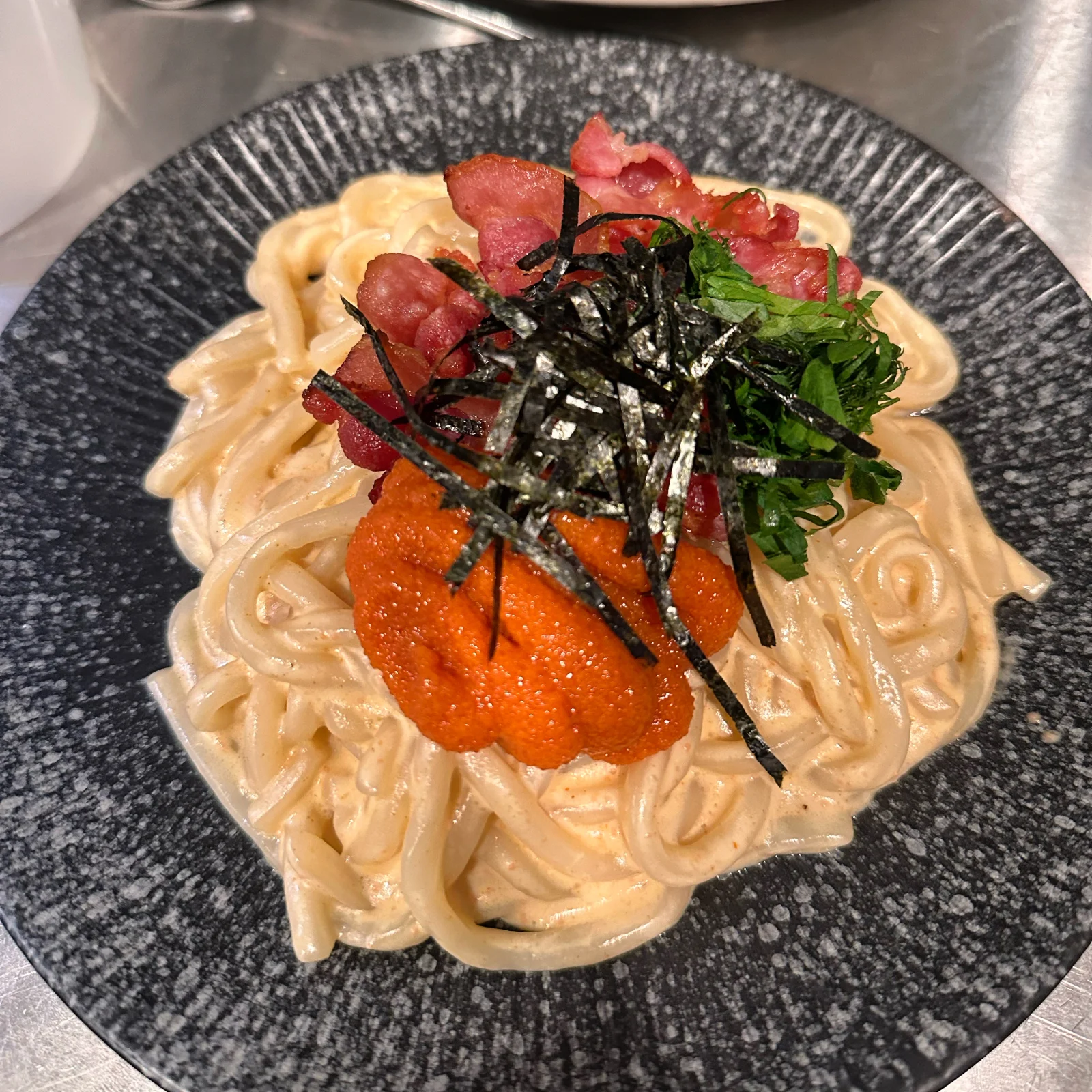 A creamy noodle dish topped with sea urchin, roe, shredded nori and a green leaf on a patterned plate.