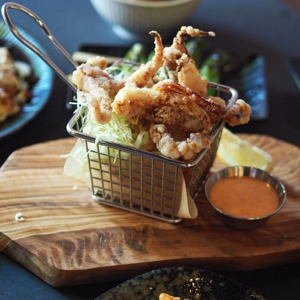 Crisp fried chicken in a small metal basket on a wooden board with dipping sauce.