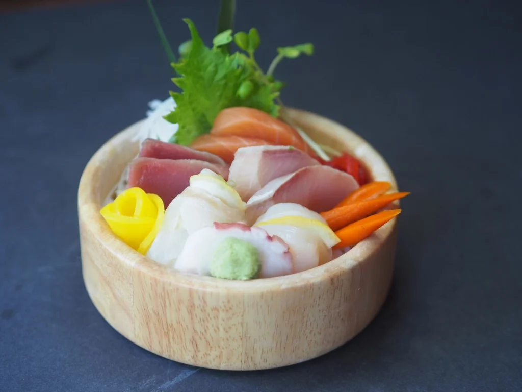 Assorted sashimi in a wooden bowl with shredded daikon, shiso and carrot garnishes.