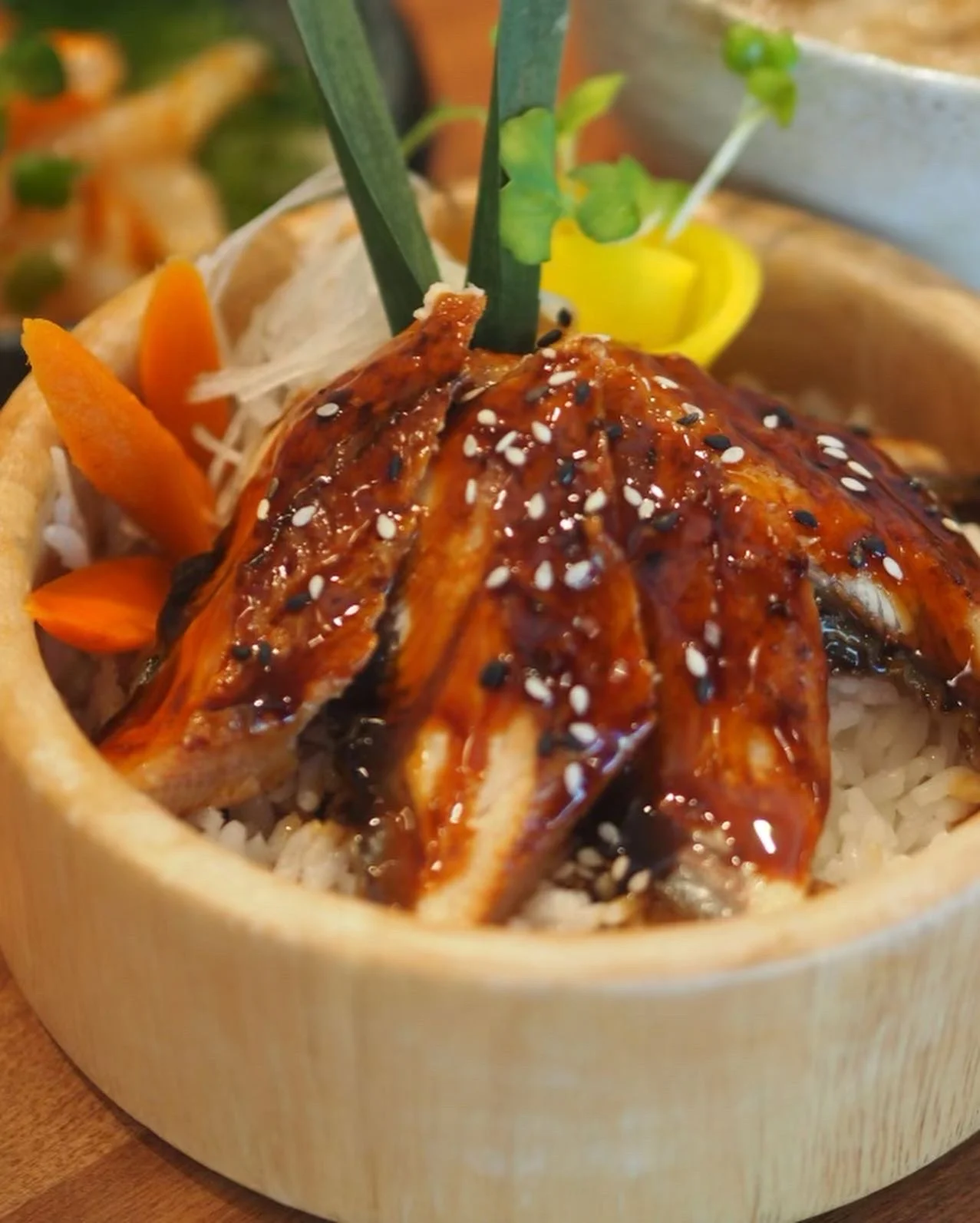 Glazed grilled eel served in a wooden bowl with shredded daikon and vegetable garnishes.