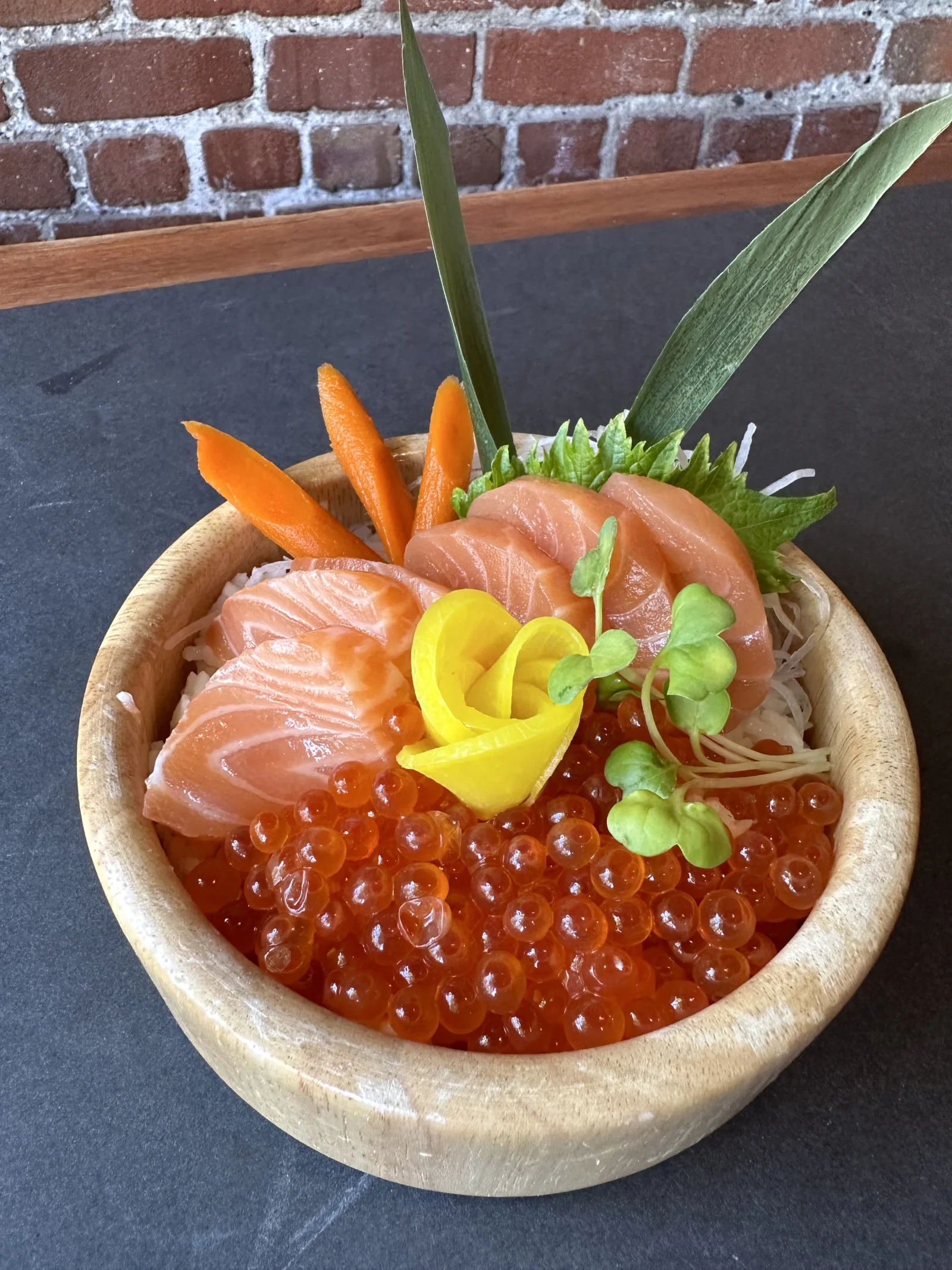 Salmon slices and roe in a wooden bowl with shredded daikon, green leaves and vegetable garnishes.